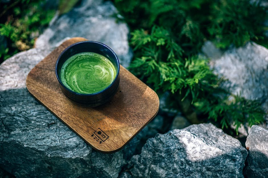 Top view of a green matcha tea served on a wooden tray outdoors, surrounded by rocks.